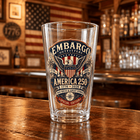 Pint glass for 250th America with Embargo Outfitters label on a wooden bar counter