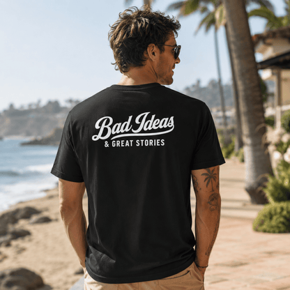 Man wearing a black t-shirt with 'Bad Ideas & Great Stories' text on a beach.