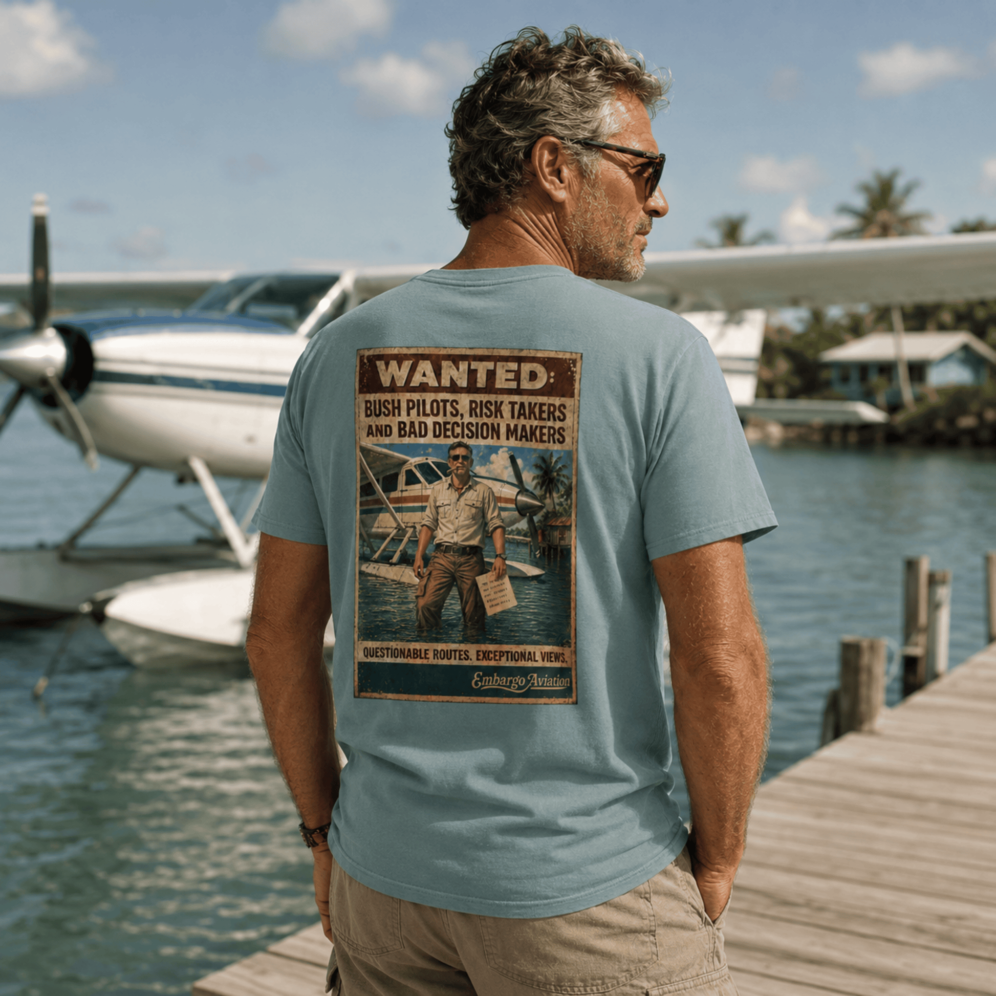 Man wearing an embargo aviation theme t-shirt, standing on a dock with a seaplane in the background.