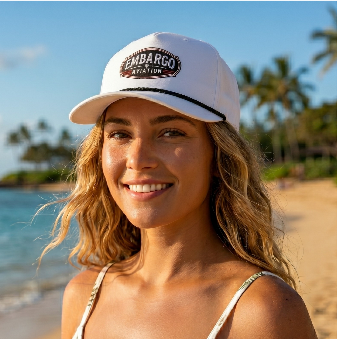Woman wearing a white cap with 'Embargo Aviation' logo on a beach