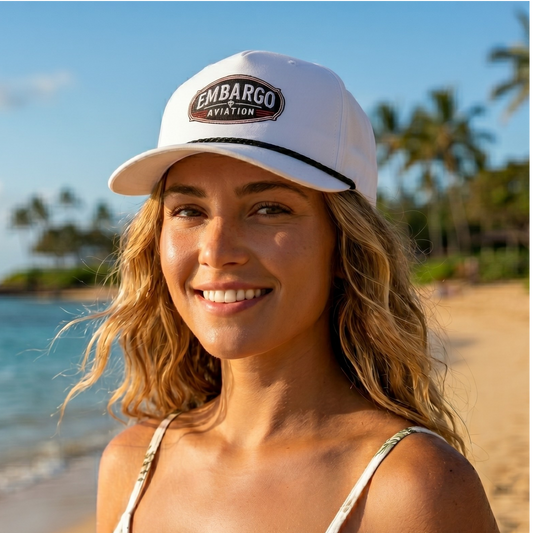 Woman wearing a white cap with 'Embargo Aviation' logo on a beach