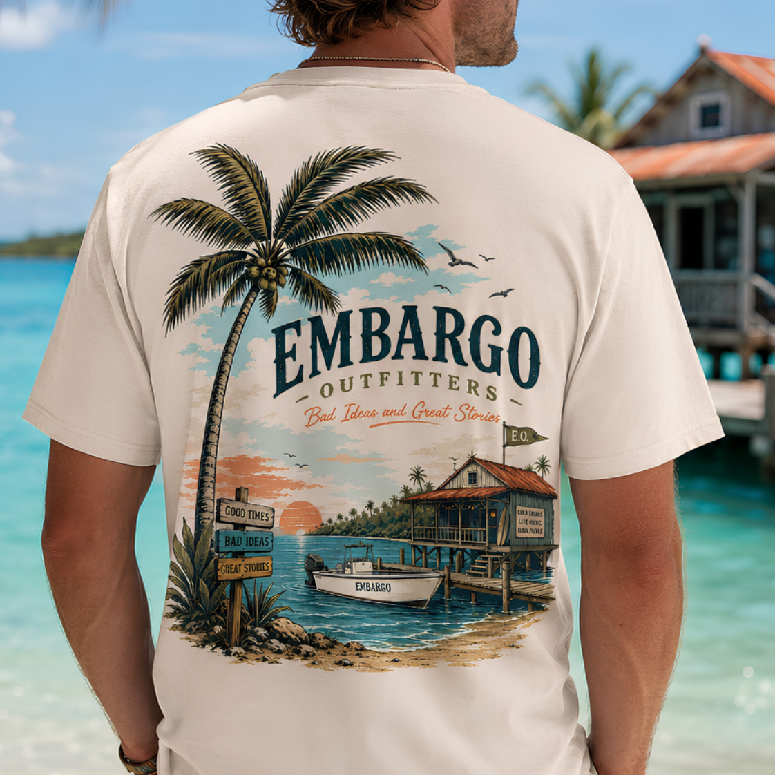 Man wearing a t-shirt with 'Embargo Outfitters' design on a beach