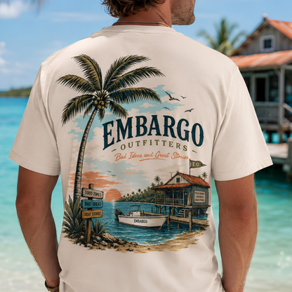 Man wearing a t-shirt with 'Embargo Outfitters' design on a beach