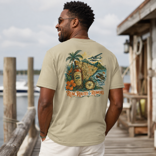 Man wearing a 'Rum, Routes & Rumors' t-shirt by a dock with water and wooden structures in the background.