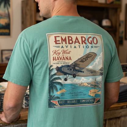 Person wearing a teal t-shirt with 'Embargo Aviation' graphic in a store setting.