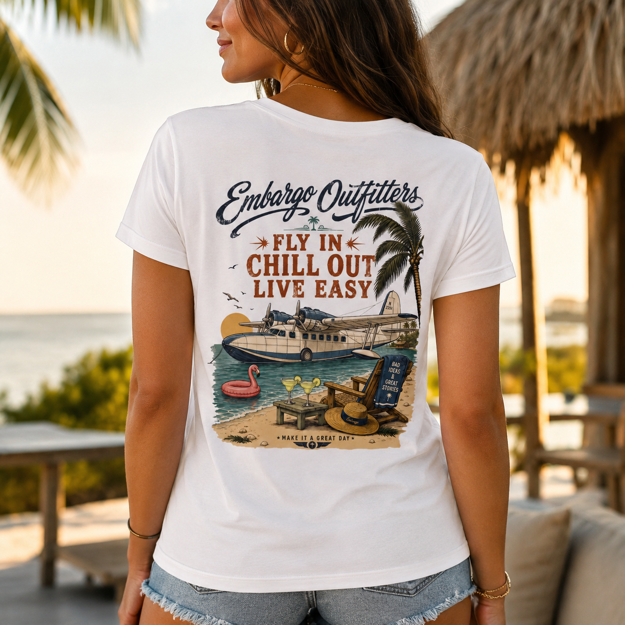 Person wearing a white t-shirt with a beach-themed graphic and text, standing in a tropical setting.